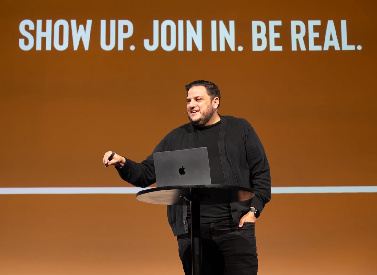 Nick Lenzi teaching on stage with 'Show Up. Join In. Be Real.' behind him
