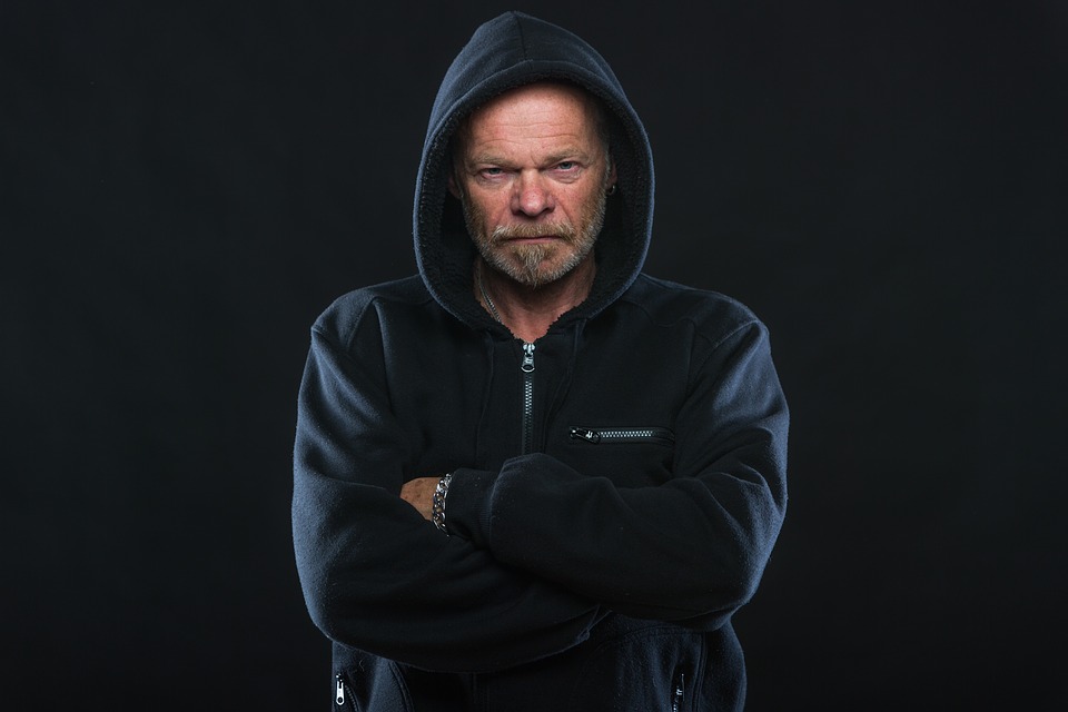 Man in a black hoodie with a serious expression, representing a lack of emotional awareness against a dark background.